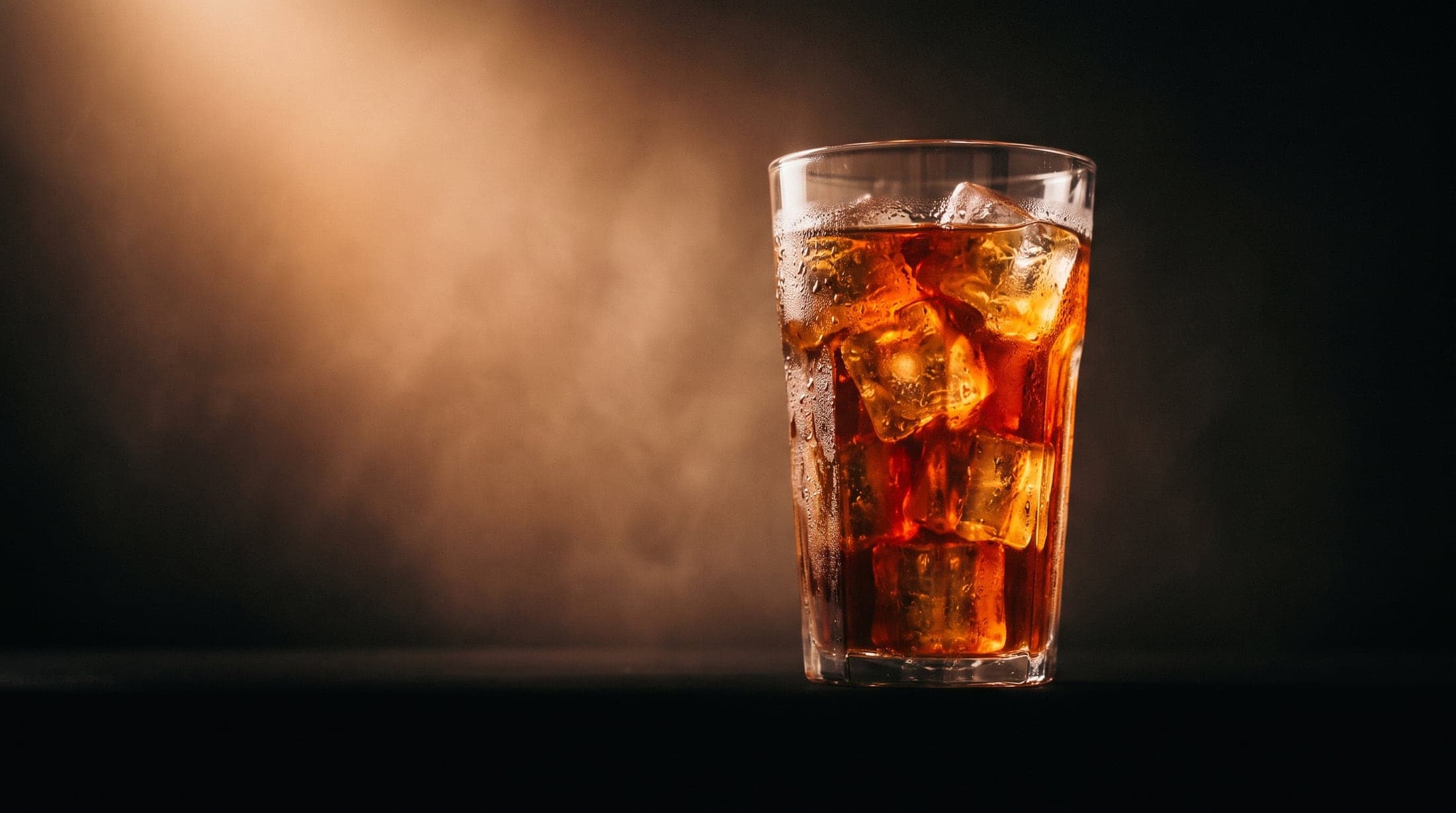 Cold brew ámbar sobre hielo, iluminado de lado.